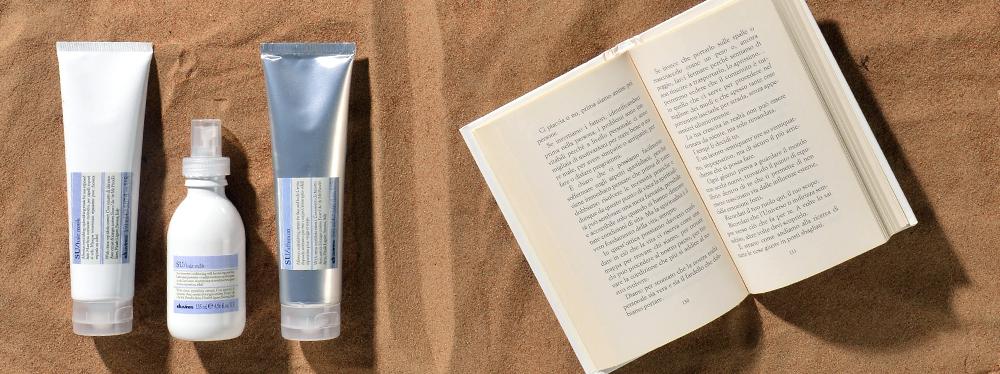 Davines Su products at the beach with a book