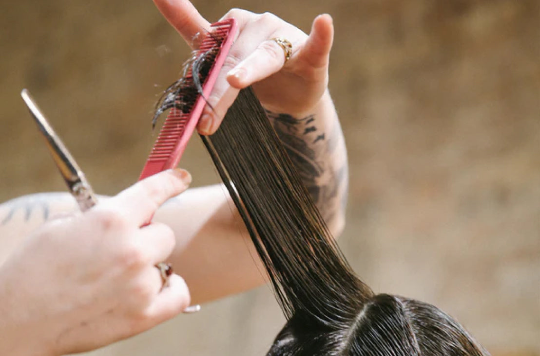 close-up of hair being cut by hands holding scissors and a pink comb
